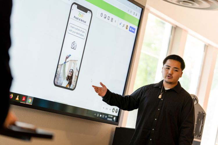 A student stands next to a projection screen with an app displayed